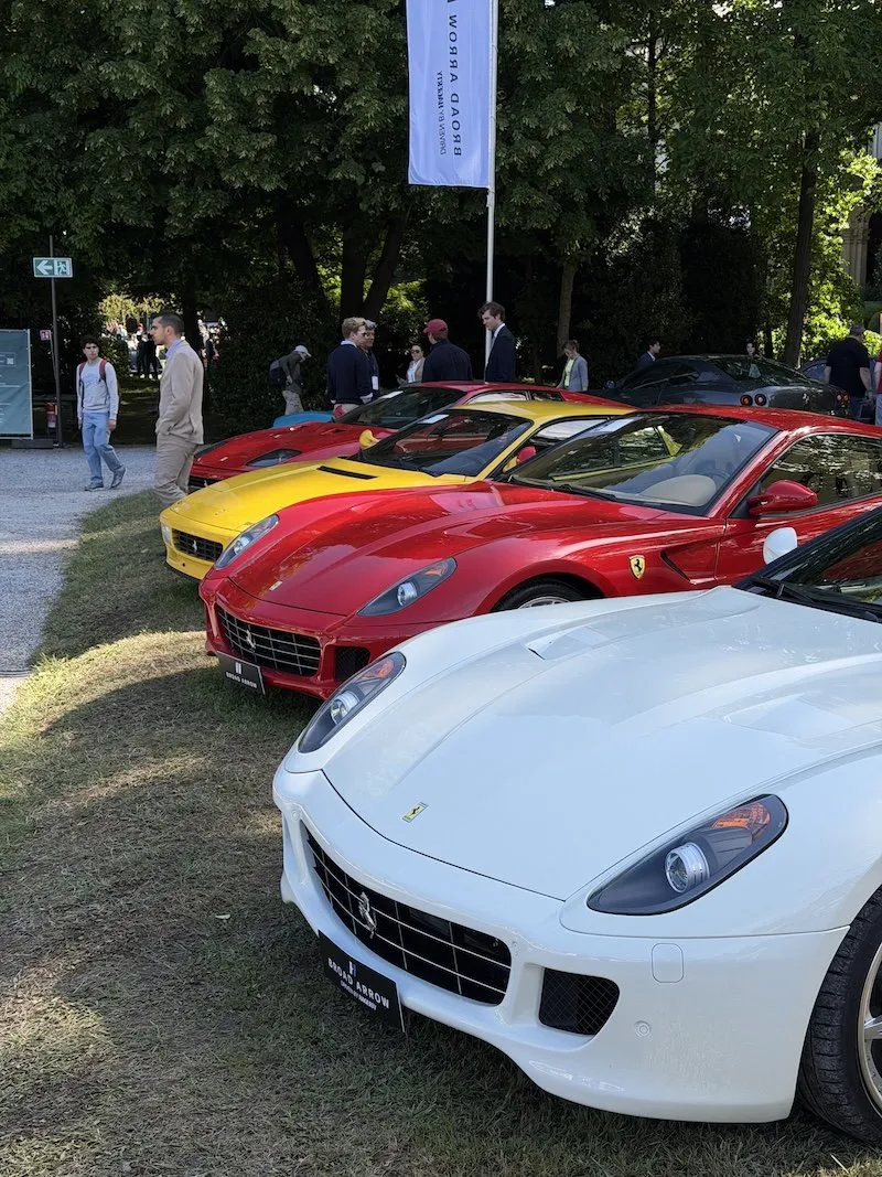 A row of Ferrari grand tourers lined up on the grass at the Concorso d’Eleganza, with visitors walking between the cars.