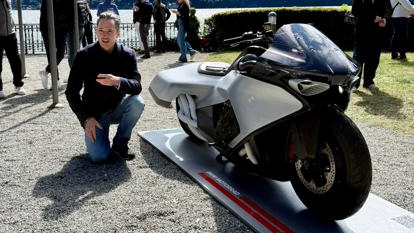 Nils kneels next to the BMW Motorrad Vision K18 concept on its display platform at the Concorso d'Eleganza, with Lake Como in the background.