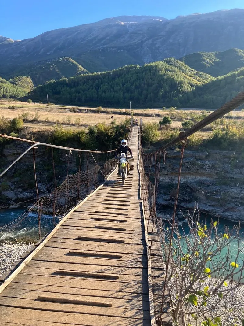Crossing a narrow suspension bridge with an enduro over a Balkan mountain river