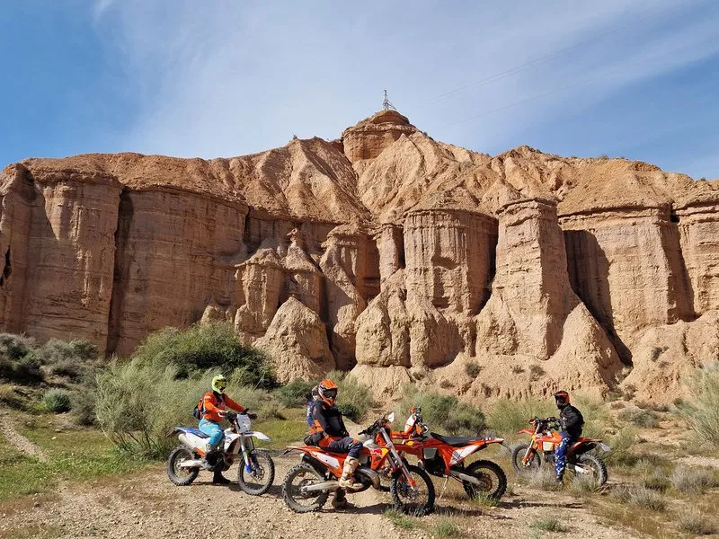 Enduro riders stopped on a dirt track in front of an eroded cliff of earth pillars.