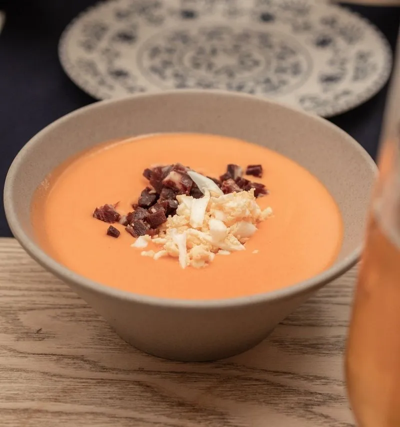 A bowl of salmorejo topped with diced ham and chopped egg.