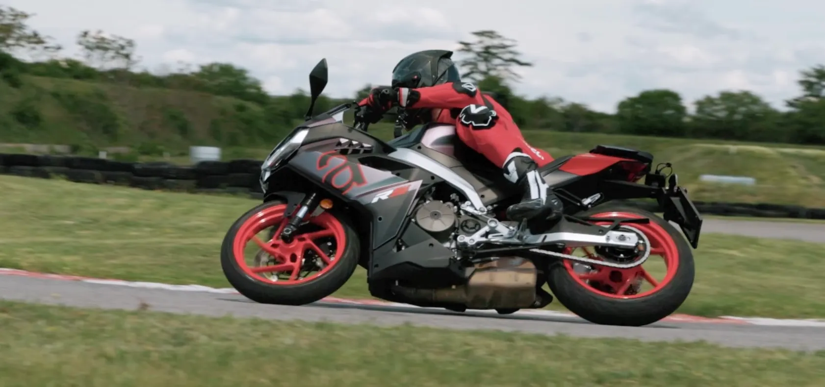 NastyNils rides the Aprilia RS 457 through a corner at the Bad Fischau supermoto circuit in Austria, wearing red Vanucci leathers and a black full-face helmet. One motorcycle and one rider are visible.