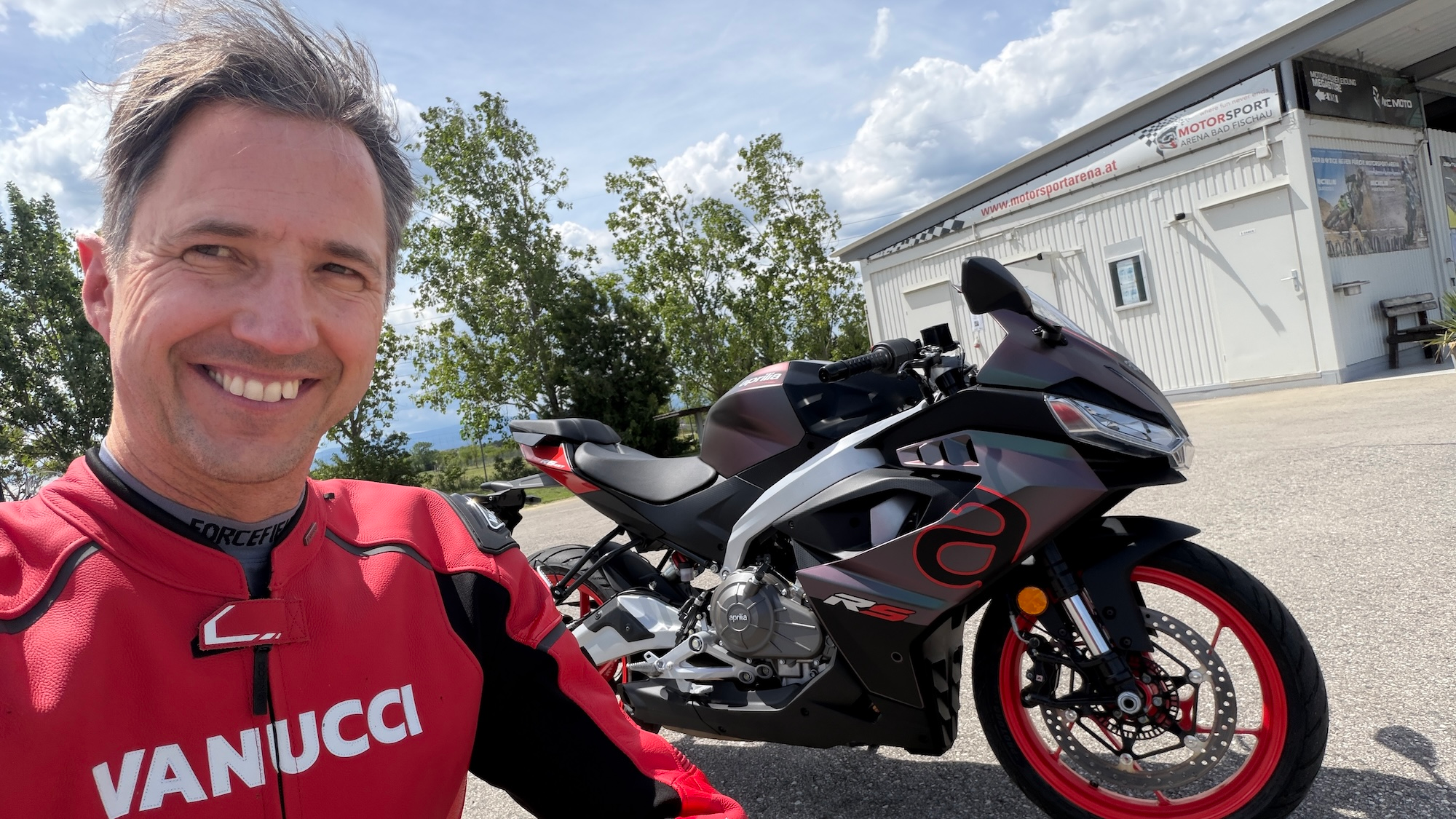 NastyNils selfie with the Aprilia RS 457 MY2026 in dark gunmetal/red colorway at Motorsport Arena Austria, Bestzeit Produktionstag.