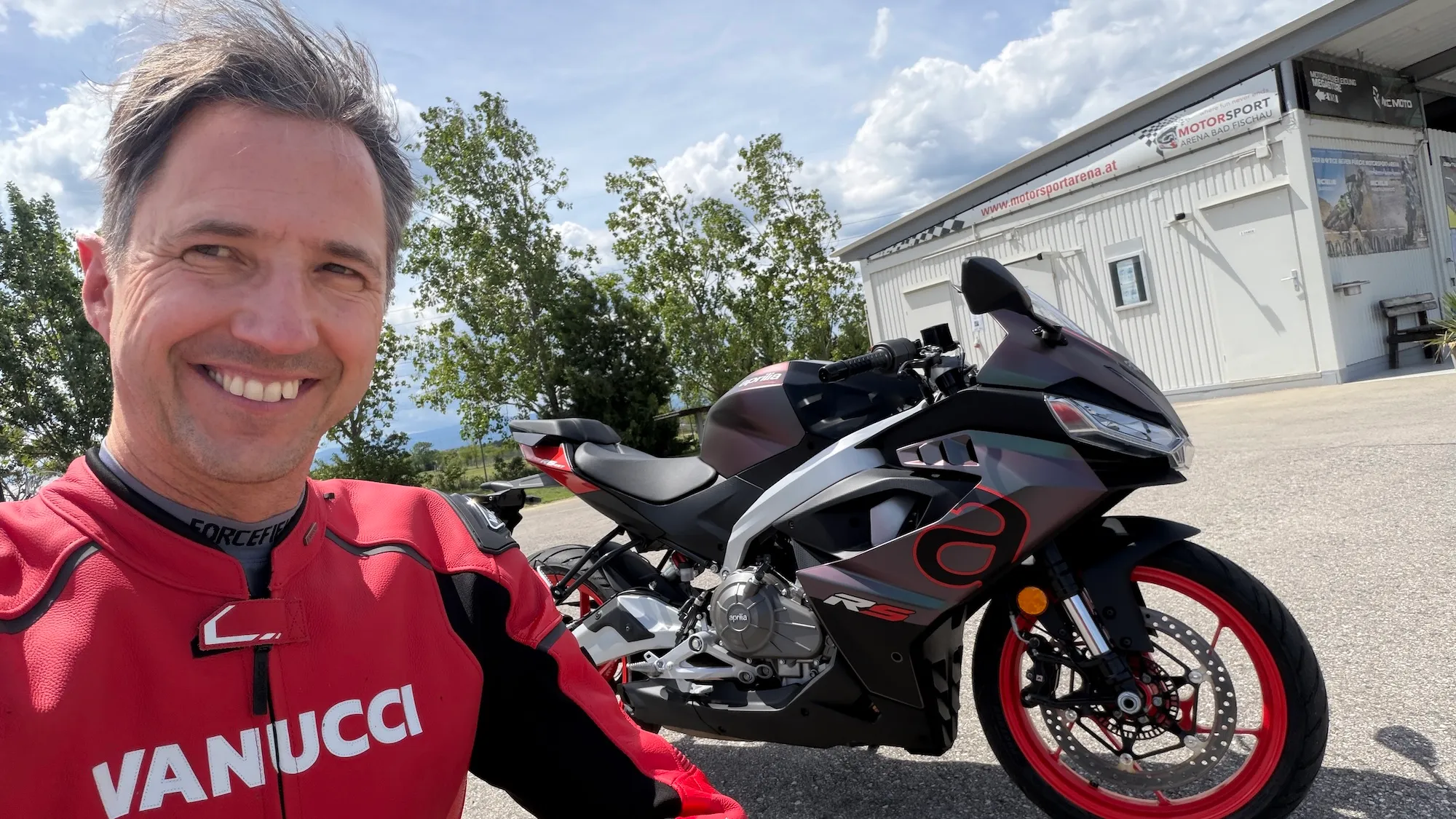 NastyNils selfie with the Aprilia RS 457 MY2026 in dark gunmetal/red colorway at Motorsport Arena Austria, Bestzeit Produktionstag.