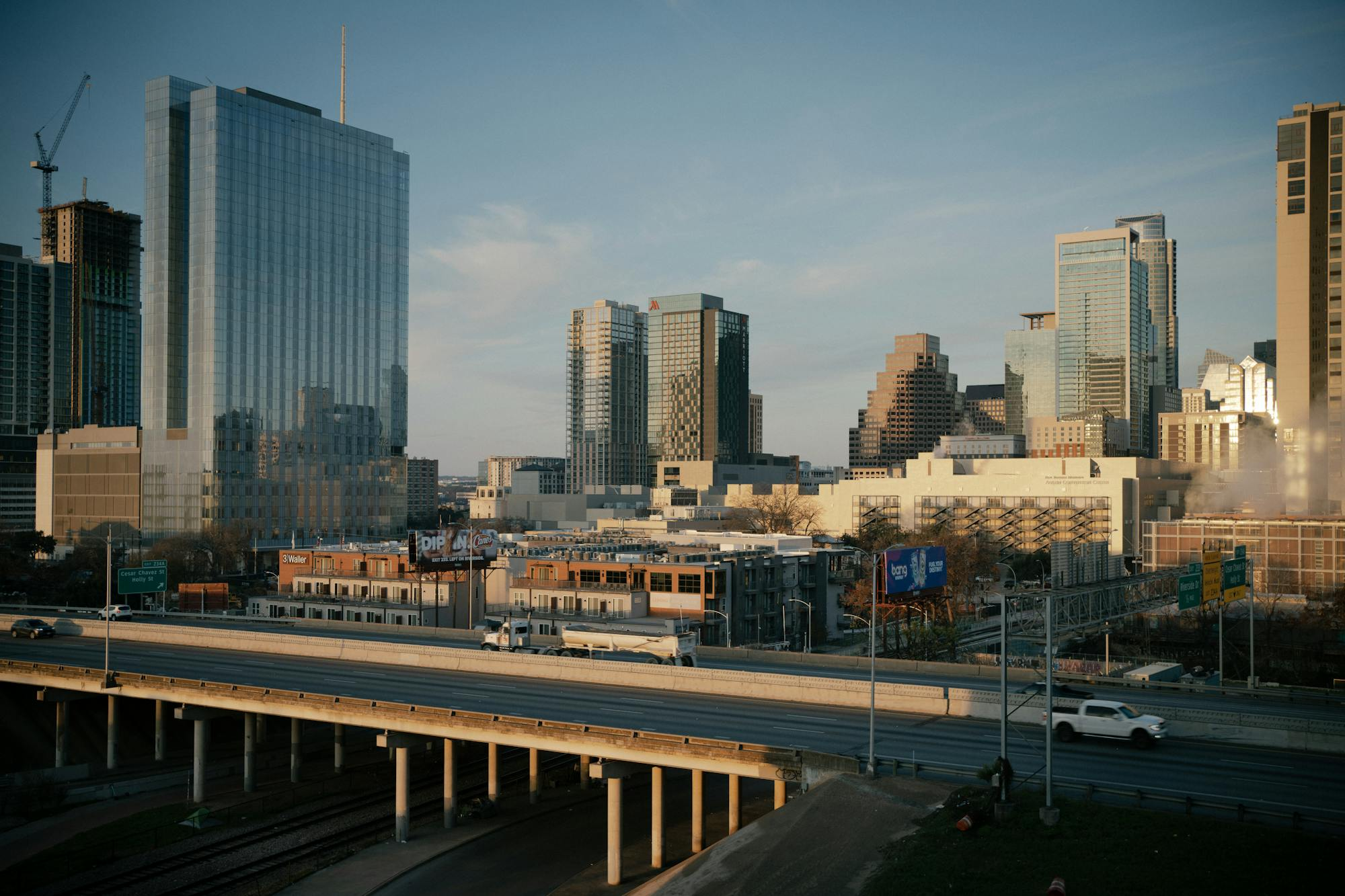 Aerial photograph of downtown Austin, Texas, showing modern high-rise buildings against a clear blue sky. Urban infrastructure, highways, and parking structures visible in the foreground. No motorcycle or person visible. Stock photography from Pexels by Thomas Balabaud.