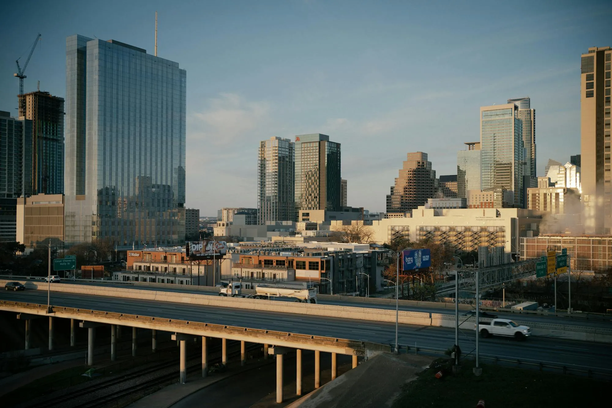 Aerial photograph of downtown Austin, Texas, showing modern high-rise buildings against a clear blue sky. Urban infrastructure, highways, and parking structures visible in the foreground. No motorcycle or person visible. Stock photography from Pexels by Thomas Balabaud.