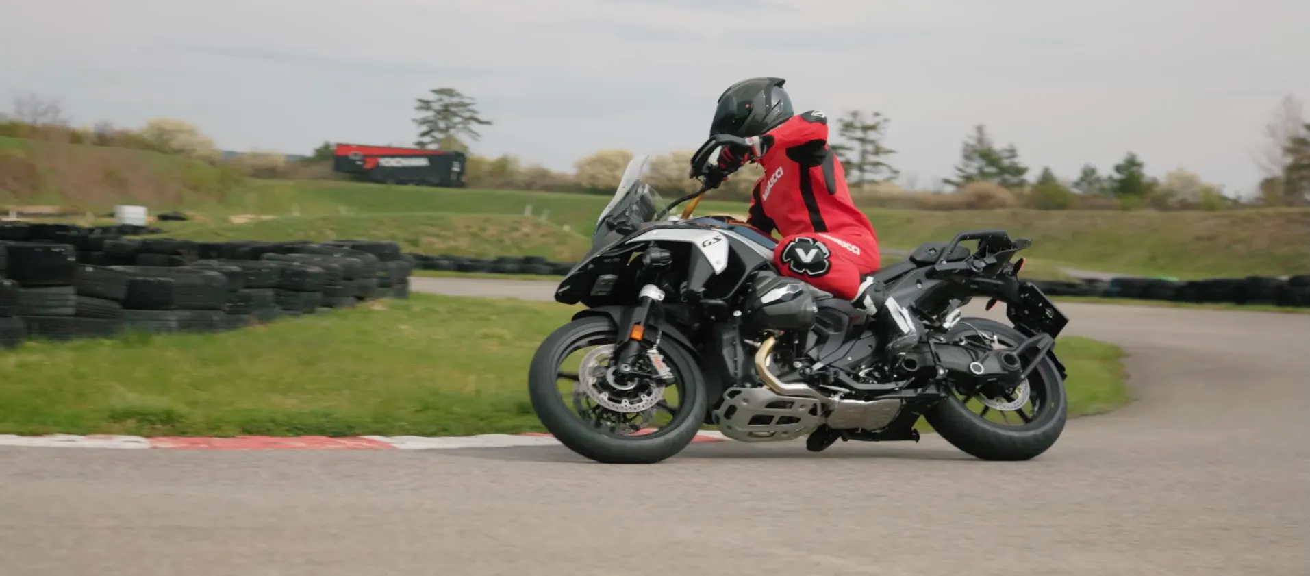 NastyNils pushes a BMW R 1300 GS hard into a tight corner on an Austrian supermoto track, the boxer cylinders and skid plate on full display as the adventure bike leans deep on dry asphalt.
