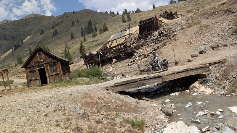 Weathered timber cabin and collapsed mill at the Animas Forks ghost town with a motorcycle on a plank bridge