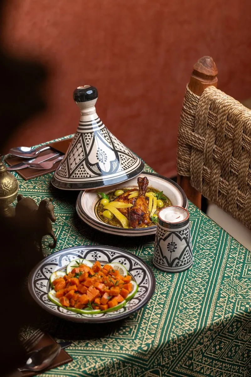 Table with a decorated tagine and plates of vegetables on a green tablecloth.