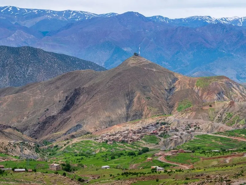 High Atlas mountains with snowy peaks above a mountain village and green terraces.