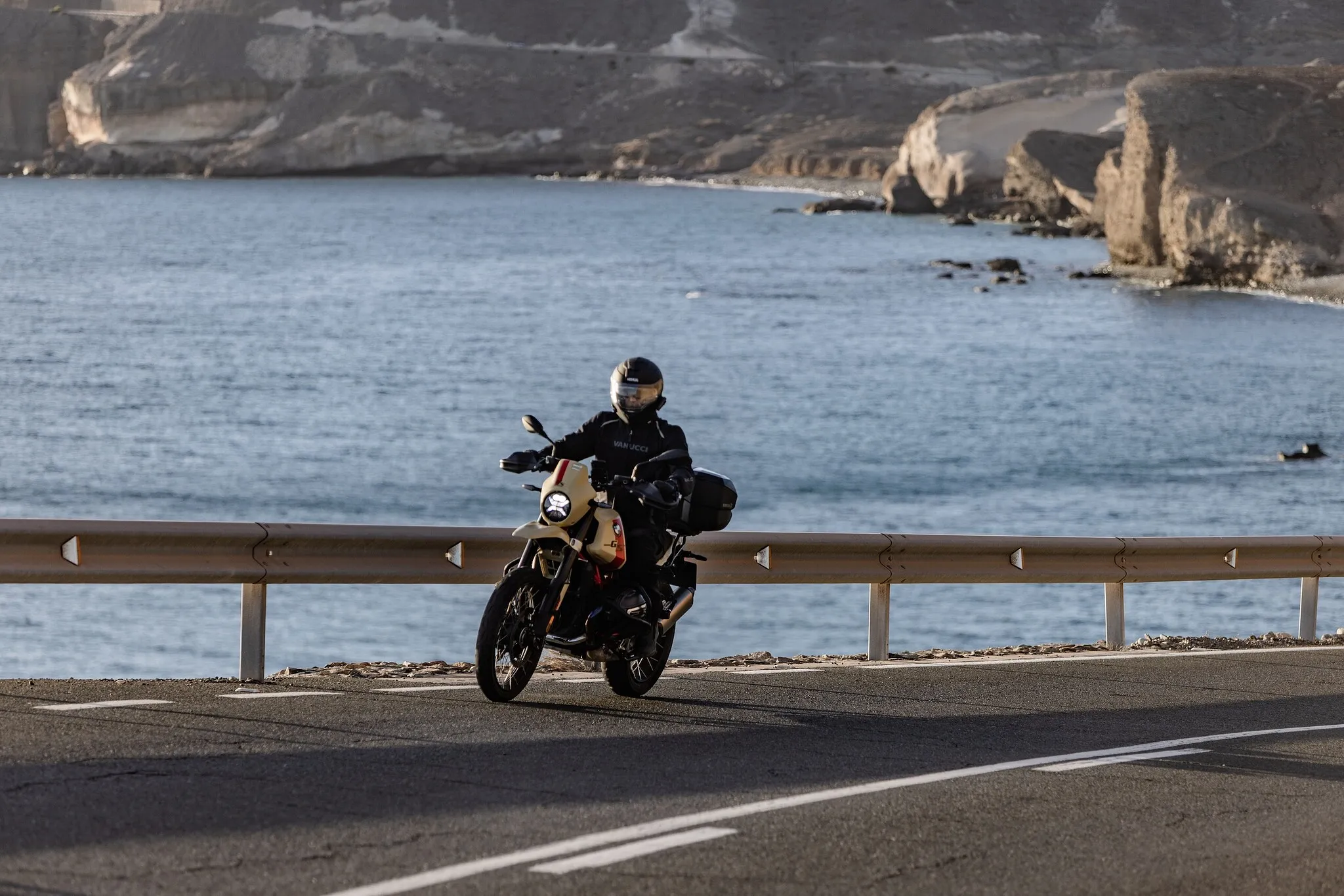 Nils on a BMW R 12 GS along a dramatic coastal cliff road — the kind of mixed-surface route where suspension travel decides whether a scrambler is real or theater.
