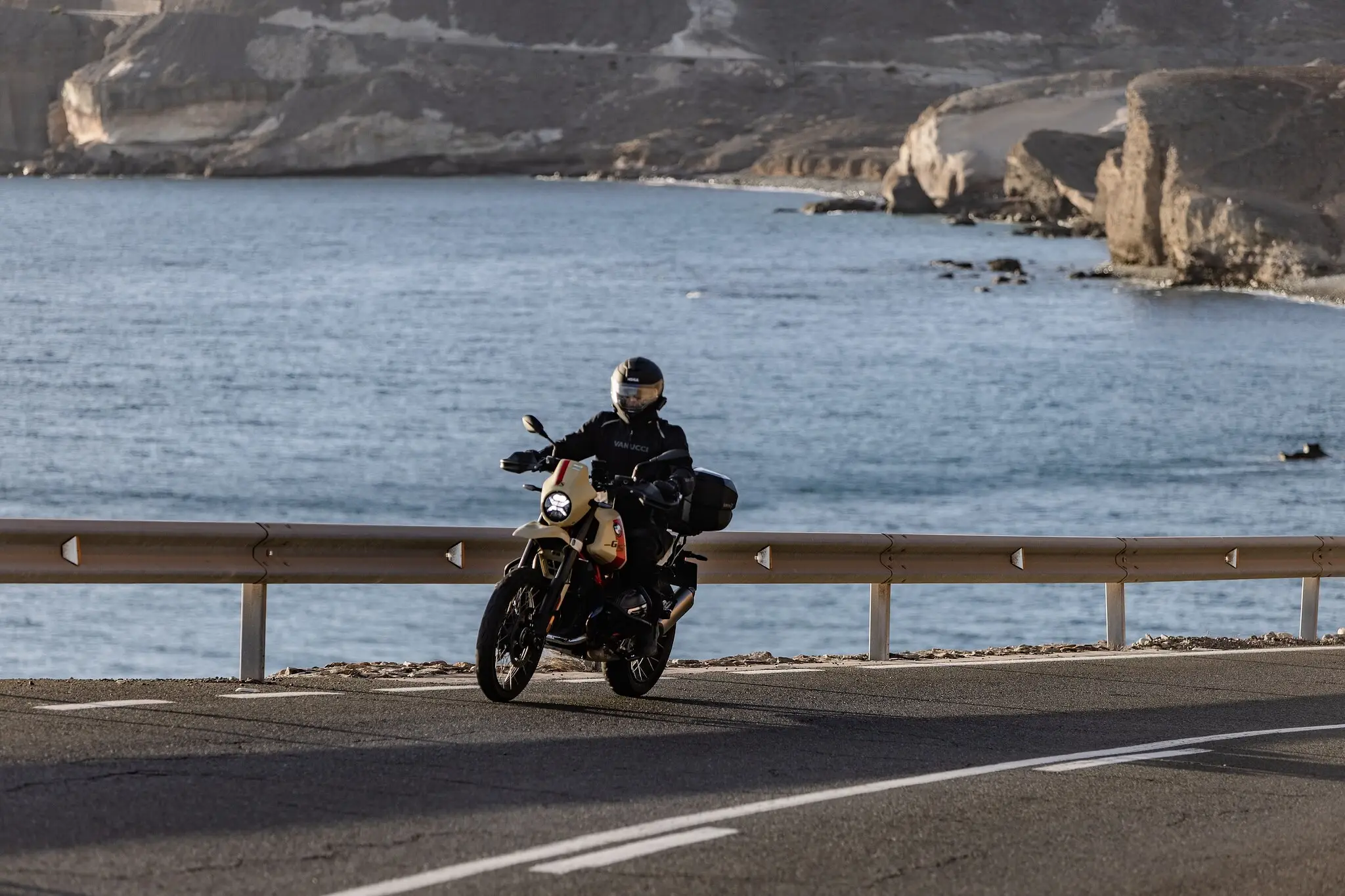 Nils on a BMW R 12 GS along a dramatic coastal cliff road — the kind of mixed-surface route where suspension travel decides whether a scrambler is real or theater.