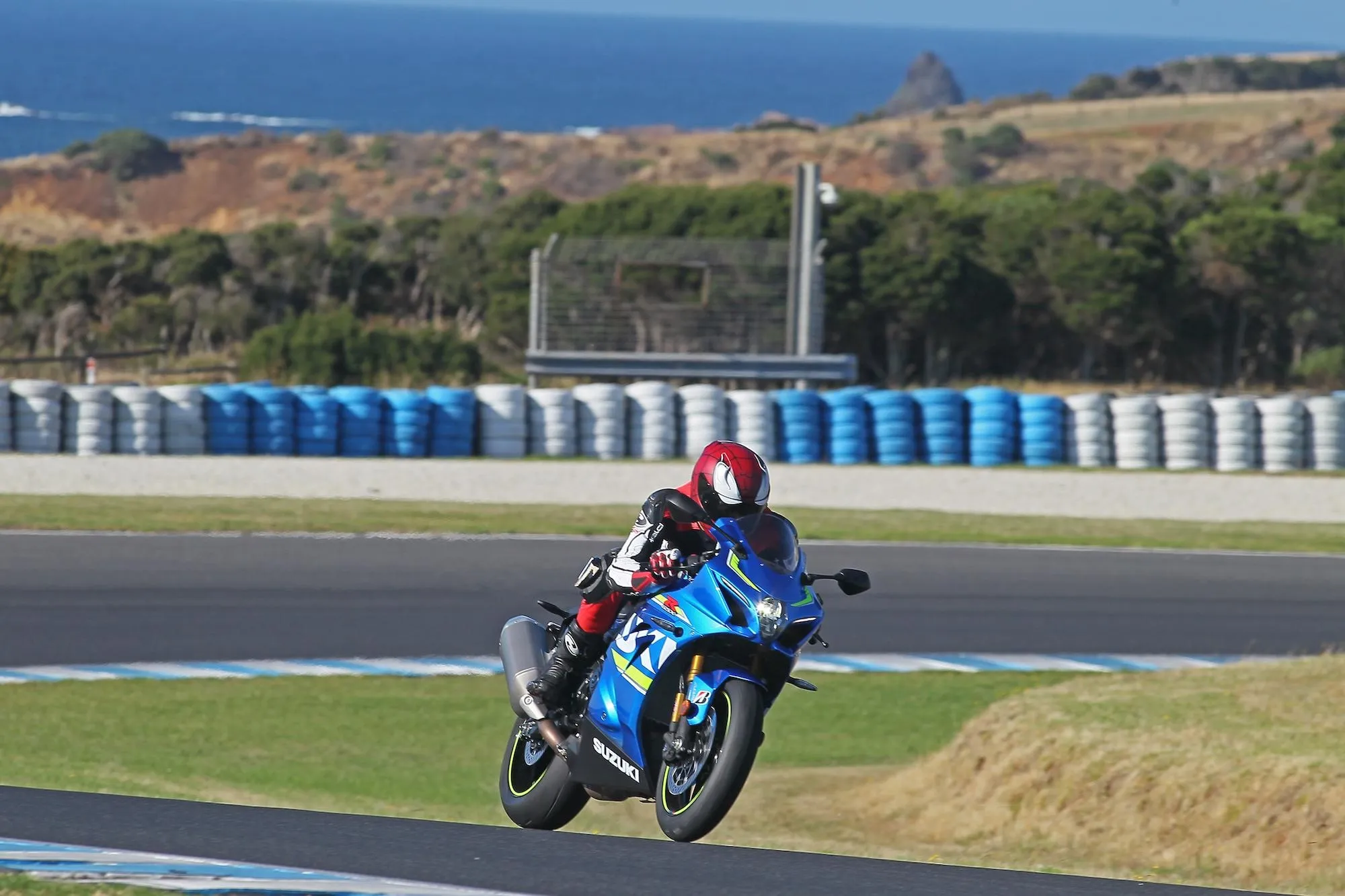 Nils on a Suzuki GSX-R1000 cornering hard at an Australian racetrack with coastal cliffs in the background — the place where lap-time obsession is loudest, and most worth quieting.