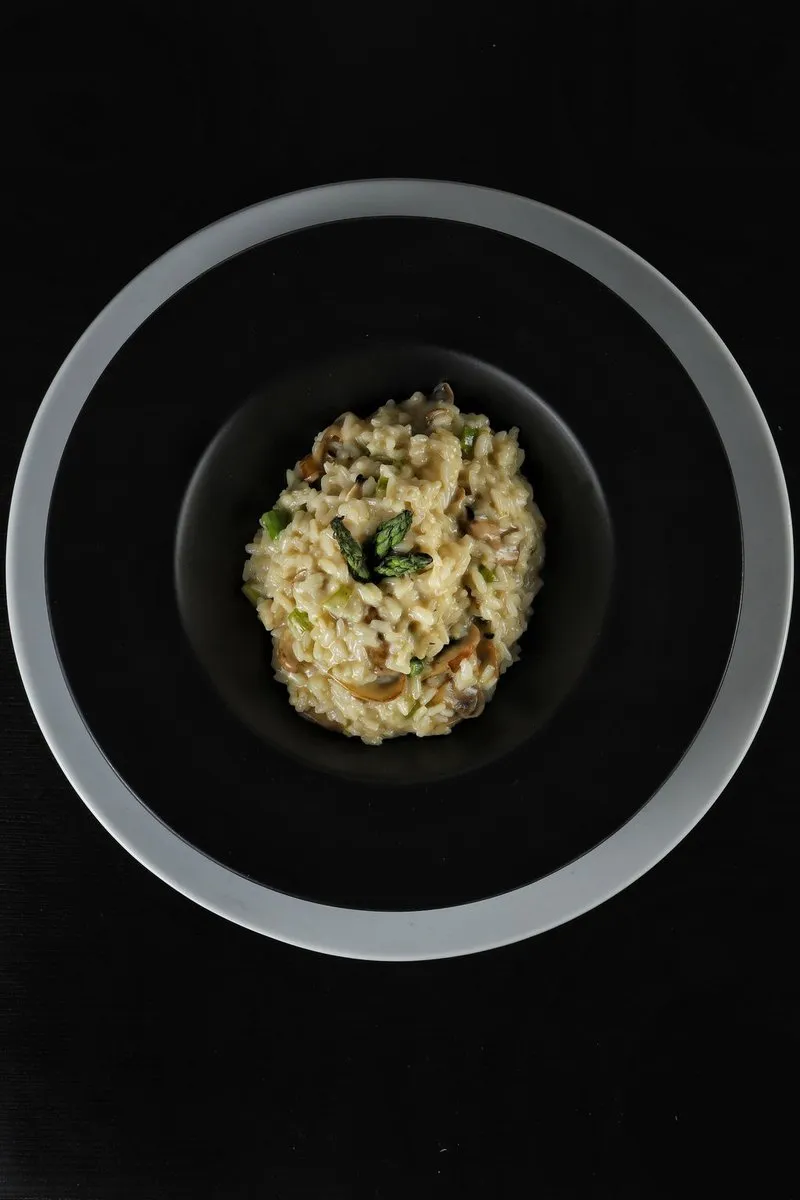 A top down view of mushroom risotto served in a black bowl on a dark table.