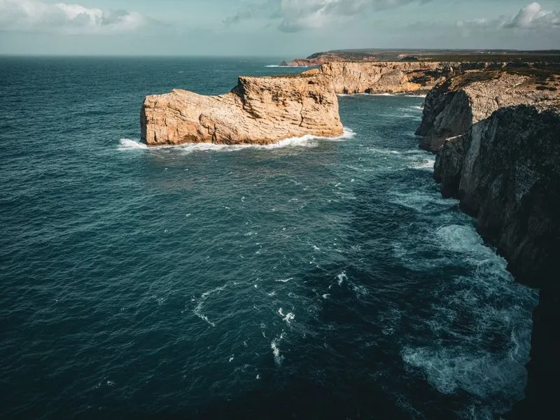 Rocky coast with cliffs and a large block of rock standing in the sea, Faro district.