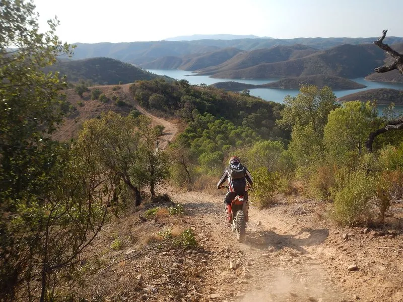 One rider on a dusty trail through scrubland, a reservoir between hills below.