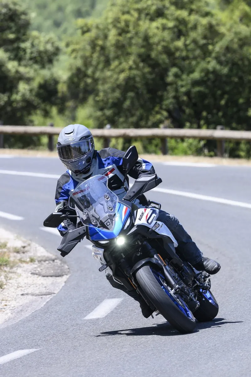 Tight cornering shot of NastyNils on the 2026 Suzuki SV7-GX, deep lean angle on a winding rural road near Montpellier during the press ride.