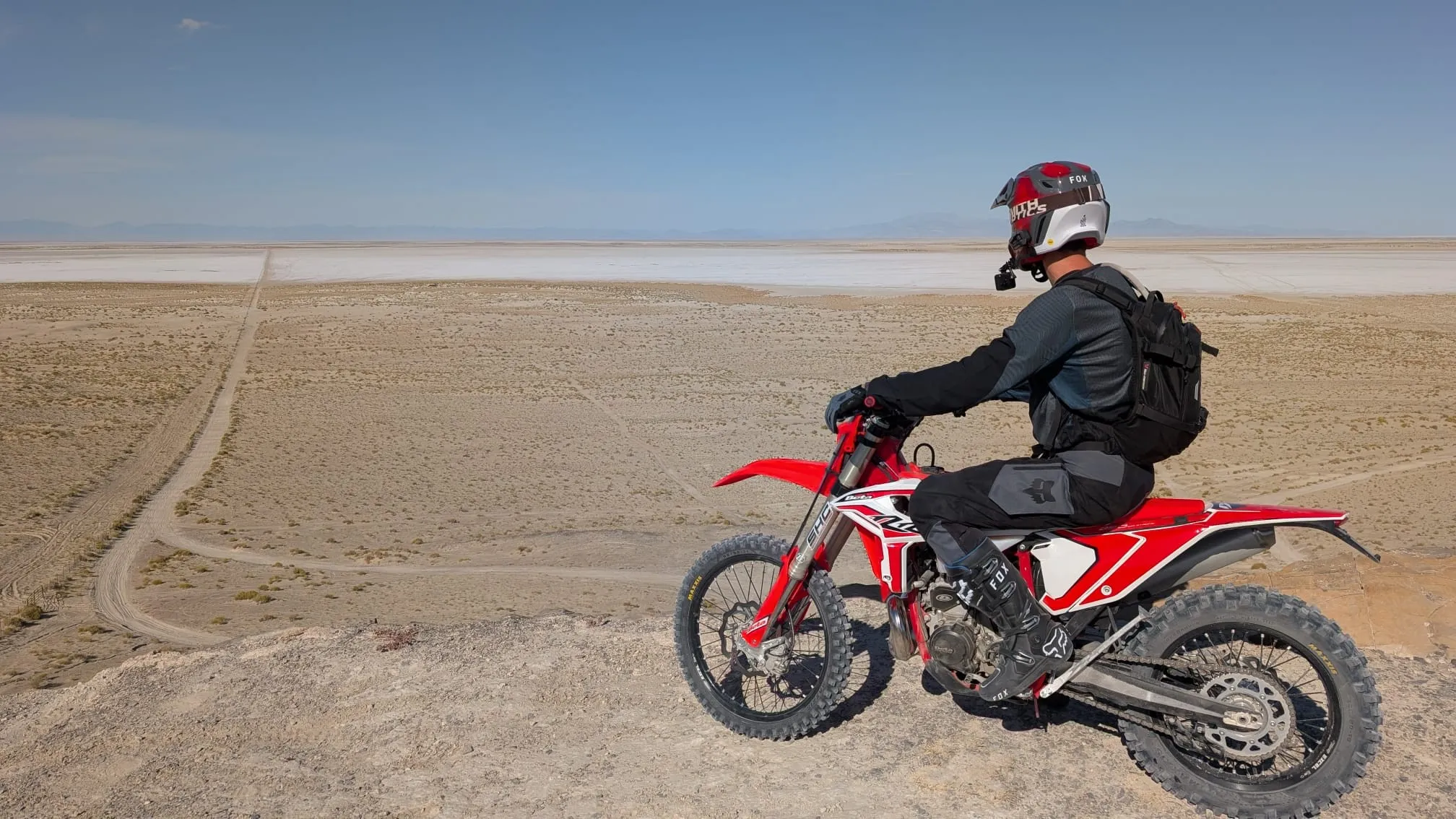 NastyNils on a red Beta RR 2T X-Pro 200 enduro on a dry dirt ridge overlooking a vast Utah salt flat with distant mountain ranges under a clear blue sky.