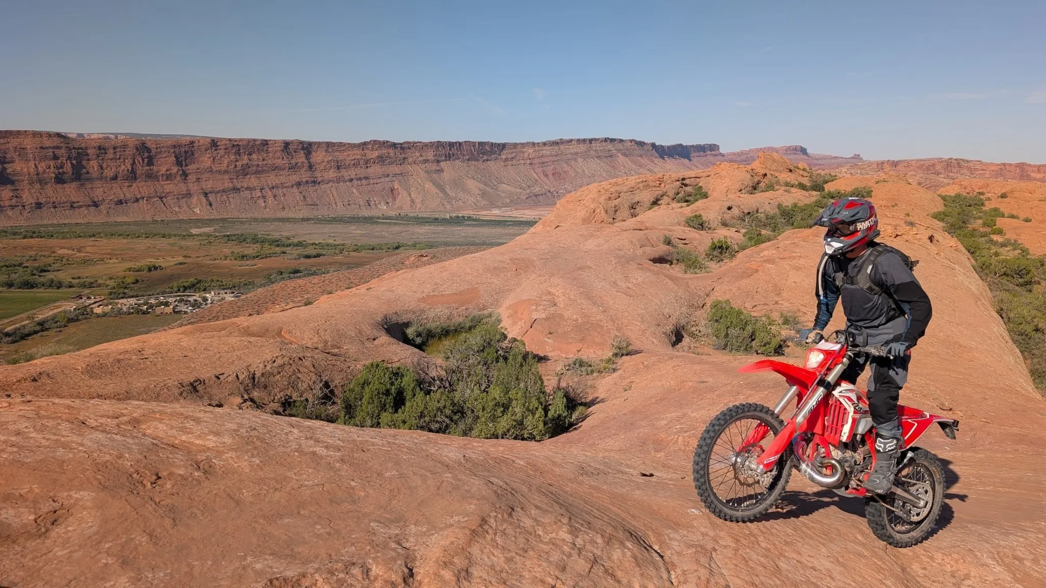 NastyNils leaning a red Beta RR 2T X-Pro 200 through a curving trail section above a Utah river valley with distant red-rock buttes on the horizon.