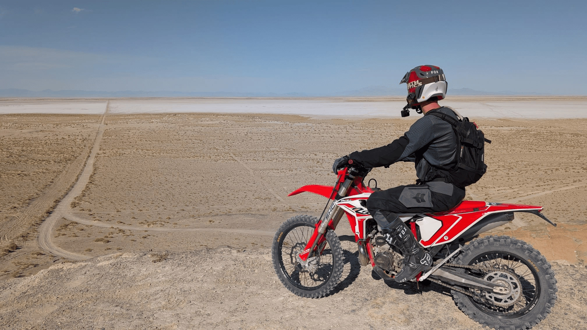 NastyNils on a red Beta RR 2T X-Pro 200 enduro on a dry dirt ridge overlooking a vast Utah salt flat with distant mountain ranges under a clear blue sky.